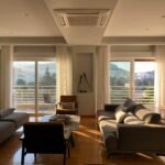 Spacious modern living room with city view and warm sunset lighting.